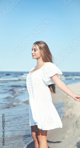 Happy, beautiful woman on the ocean beach standing in a white summer dress, open arms © rogerphoto