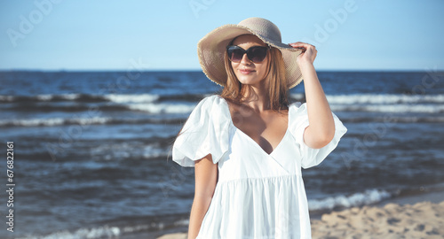 Happy blonde woman is posing on the ocean beach with sunglasses and a hat. Evening sun © rogerphoto