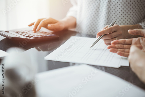 Woman accountant using a calculator and laptop computer while counting and discussing taxes with a client. Business audit and finance concepts