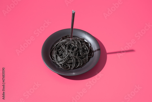 Espaguetis con tinta de calamar negro en un plato con tenedor sobre fondo rosa photo