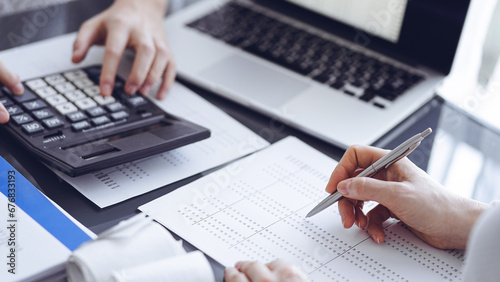 Woman accountant using a calculator and laptop computer while counting taxes for a client. Business audit concepts