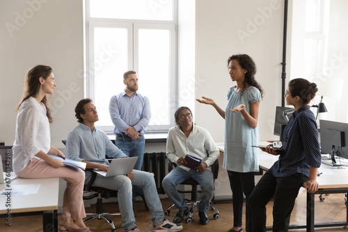 Serious African American business team employee making report to colleague on office meeting. Project leader speaking before group. Company teacher training new workers, explaining tasks