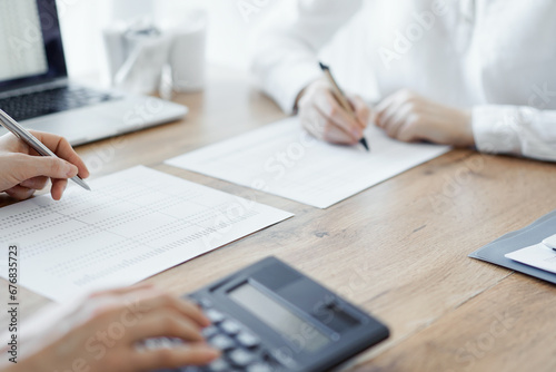 Two accountants using a laptop computer and calculator while counting taxes at wooden desk in office. Teamwork in business audit and finance