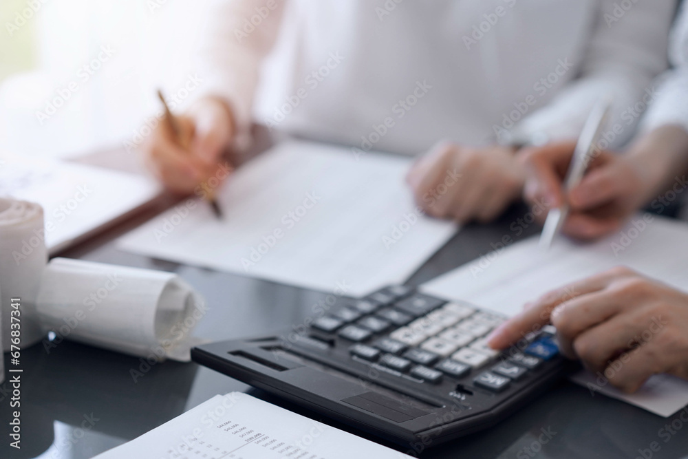 Two accountants use a calculator and laptop computer for counting taxes or revenue balance. Business, audit, and taxes concepts Two accountants use a calculator and laptop computer for counting taxes or revenue balance. Business, audit, and taxes concepts