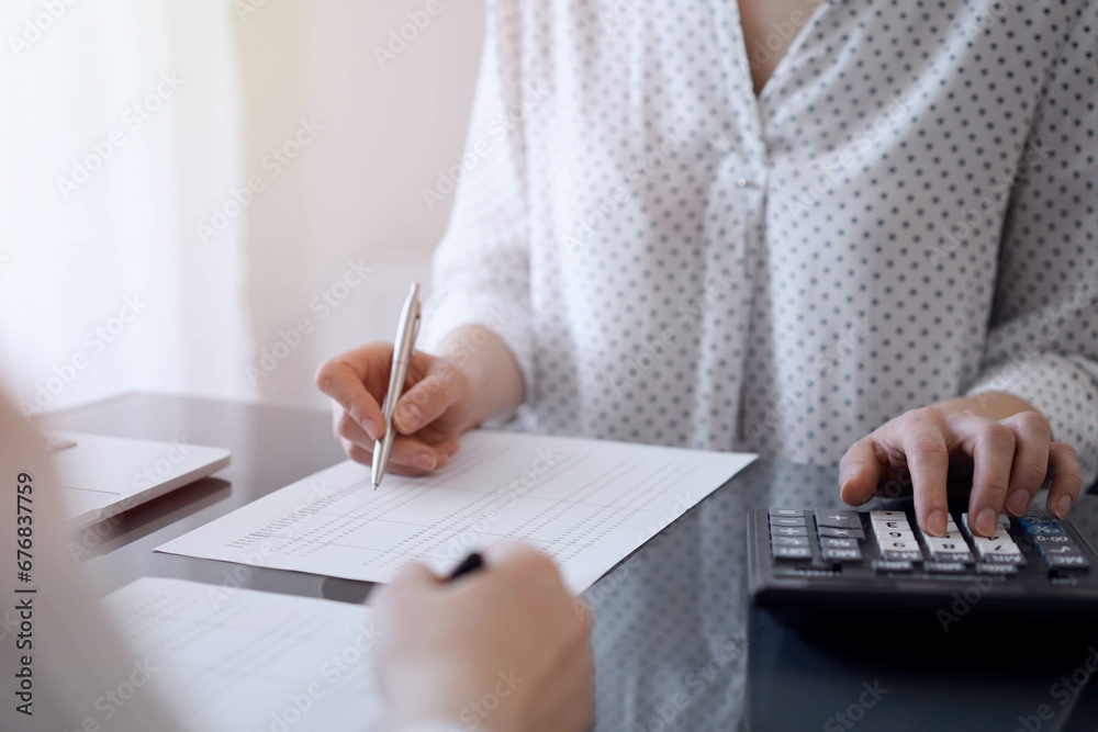 Two accountants use a calculator and laptop computer for counting taxes or revenue balance. Business, audit, and taxes concepts Two accountants use a calculator and laptop computer for counting taxes or revenue balance. Business, audit, and taxes concepts