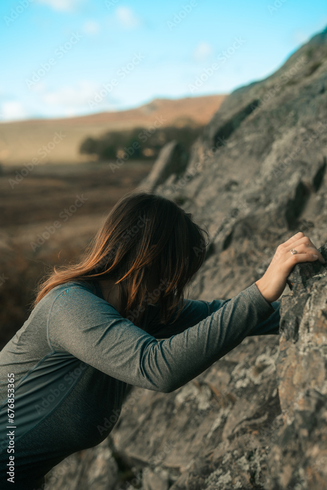Naklejka premium Rock climbing lady, woman mountain climbing wearing a long sleeve sports shirt, gripping rocks, bouldering outdoor sports and activities