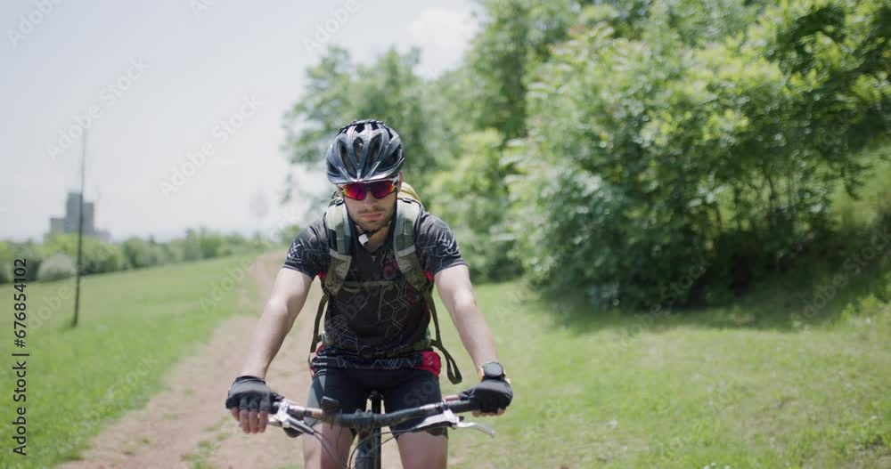 Man riding a mountainbike on a dusty path with scenic countryside background. Front view portrait. Dirtroad next to a green meadow.