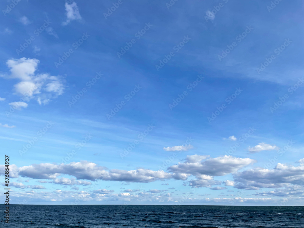 Obraz premium Seascape. Dark turquoise sea with small waves and a bright blue sky with white clouds. The horizon line is visible in the distance. Sunny autumn day.