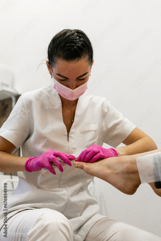 Pedicure master in medicine mask filing nails of feet. Woman legs In a