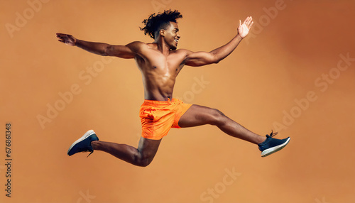 Athletic man jumping in dynamic pose, dance, wearing orange shirt and pants, yellow background, studio portrait