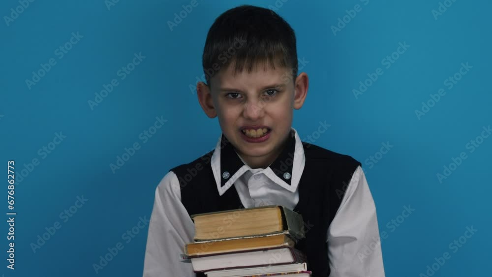 Portrait of an angry boy looking at the camera. Aggressive schoolboy gets angry in front of the camera and holds a stack of books. School everyday life concept.