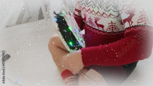 Close-up of man wrapping spool of glowing garland while removing decorations from a party until the next New Year. Sitting on the floor in red sweater.