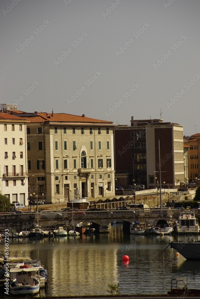 Obraz premium Vertical shot of the boats on the harbor with buildings in the background in Livorno, Italy