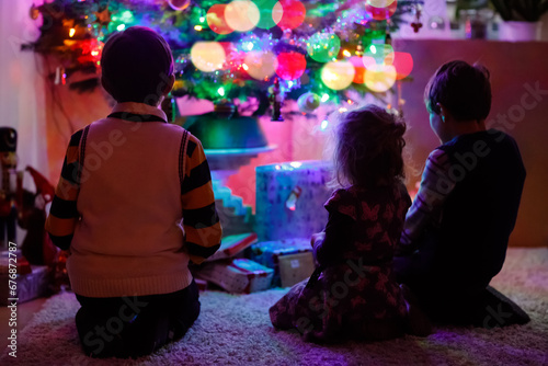 Two little kid boys and adorable toddler girl sitting by Christmas tree with old vintage toys and balls with lots of present on Xmas eve. Family preaparation celebration of family feast © Irina Schmidt