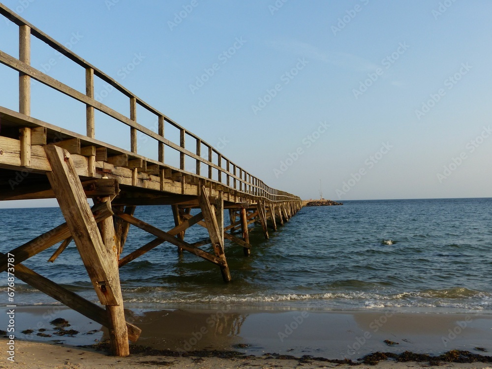 Long boardwalk extending from the coastline into the sea with a clear sky background