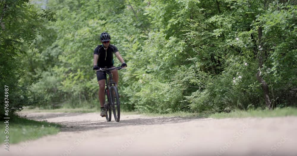Man riding a mountainbike up a dusty dirtroad path with green forest background. Front view. 50 fps on cinema camera. Man riding a mountainbike up a dusty dirtroad path with green forest background. Front view. 50 fps on cinema camera.