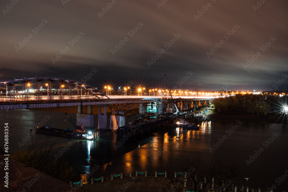 Night photo of a road bridge over a river, a cityscape, the light of street lamps on the road.
