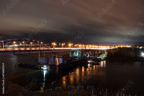 Night photo of a road bridge over a river, a cityscape, the light of street lamps on the road. © Aleksey