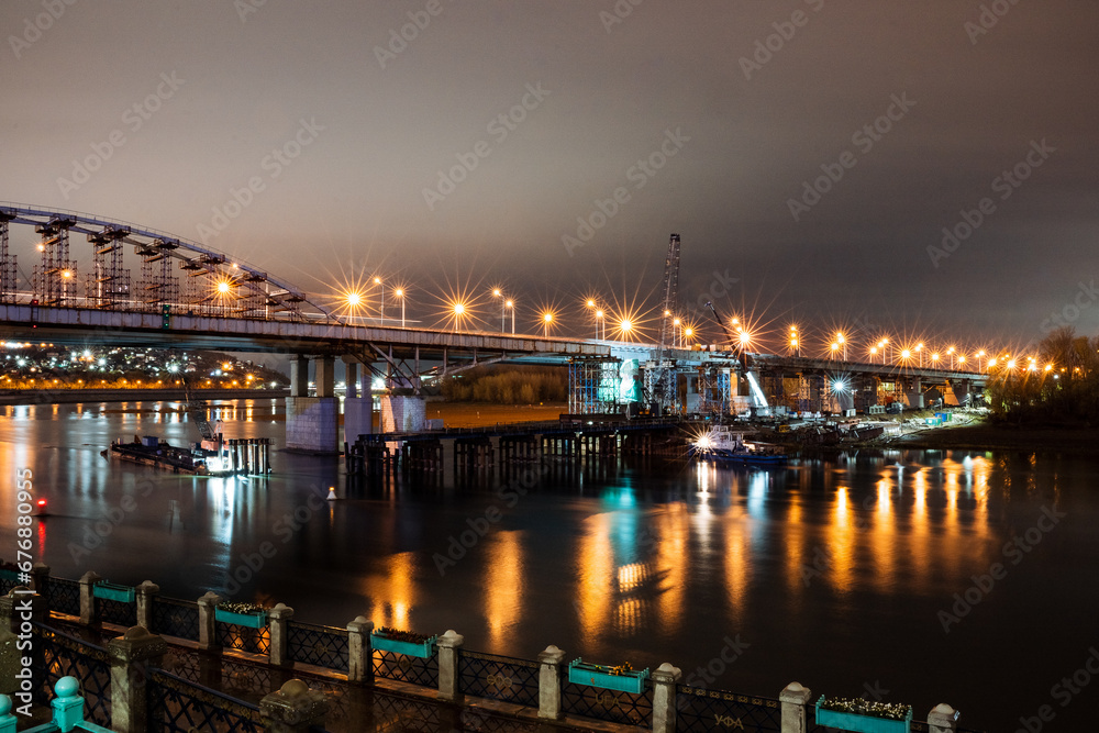 Night landscape of the city bridge over the river, lights of the evening city, the light of lanterns in the night.