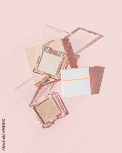 Two powder makeup highlighters on pink background with packaging