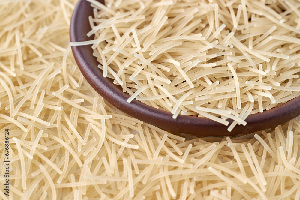 Small milk noodles in a brown clay bowl against a background of noodles scattered around. Top view with copy space