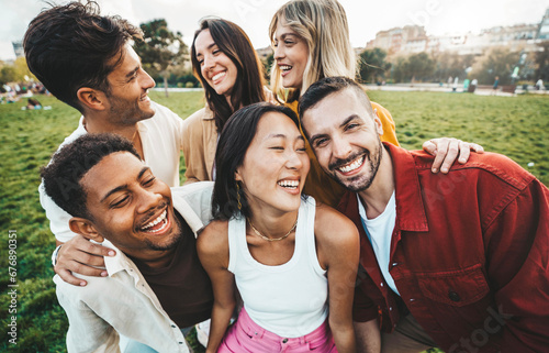 Multiracial young people laughing together outside - Happy friends having fun hanging out on summertime - Friendship concept with guys and girls hangout at the park © Davide Angelini