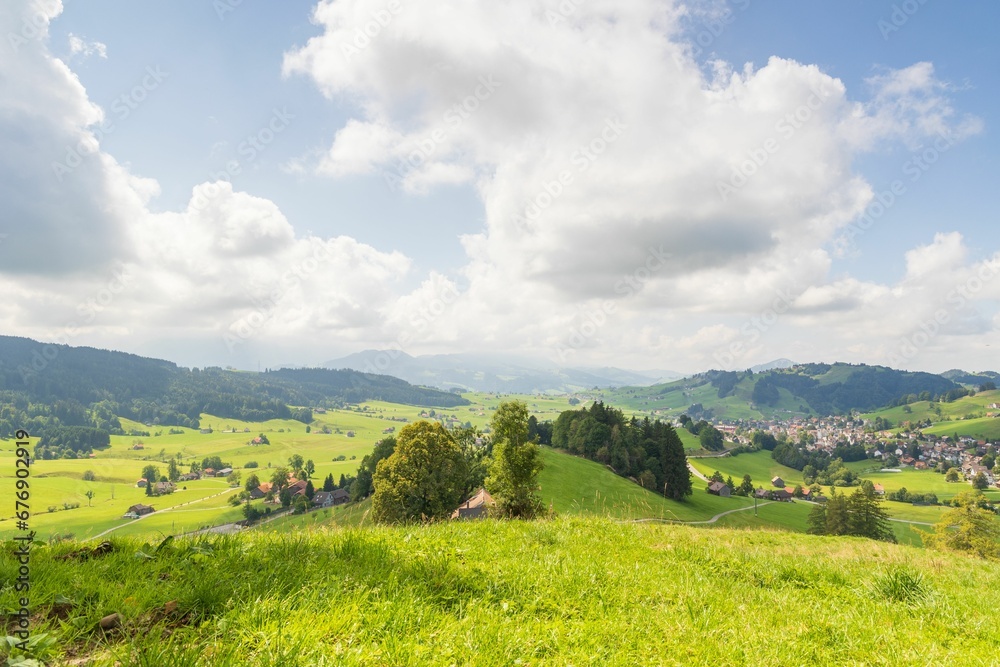 Landscape over the village in green valley surrounded by high hills under blue sky with white clouds