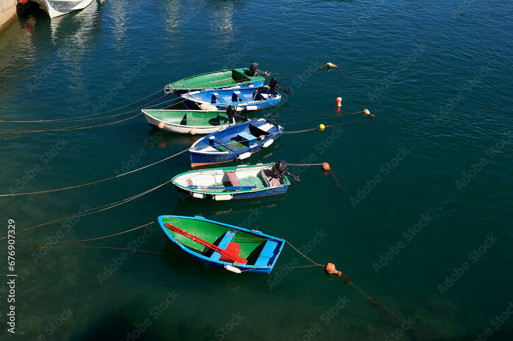 small brightly colored boats with oars and outboard motor moored with buoys in the port