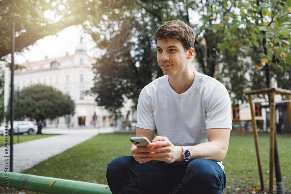 Obraz premium Young adult student using smart phone in park while going to school campus. Connected with friends everywhere, checking online bank, posting stories.
