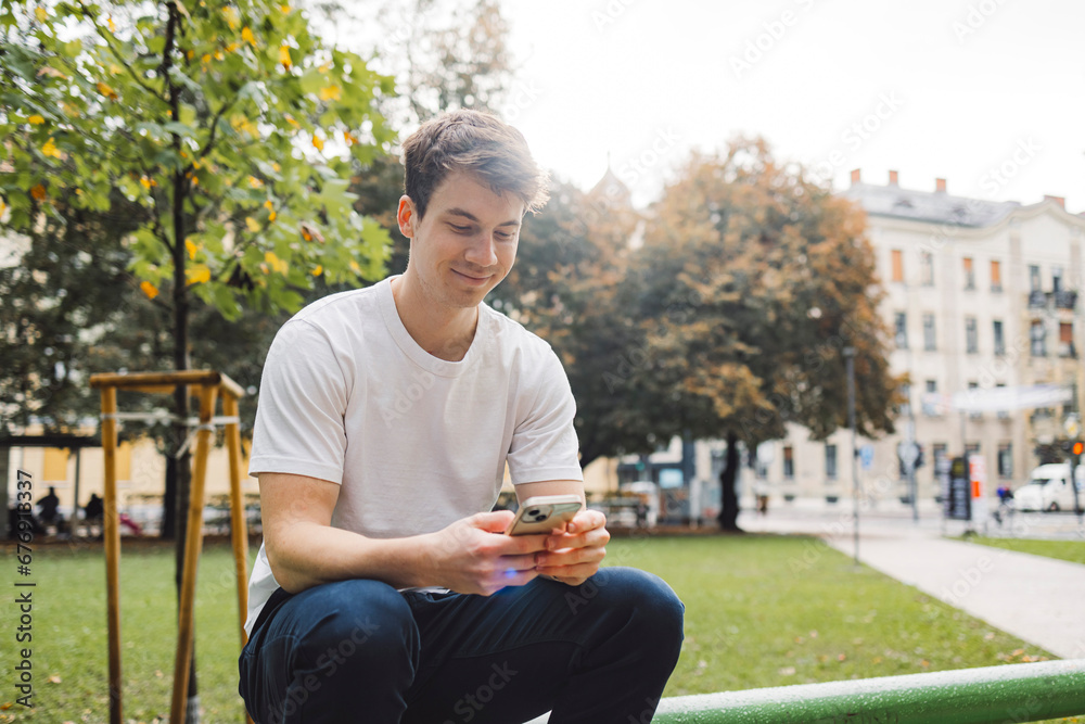 Obraz premium Young adult student using smart phone in park while going to school campus. Connected with friends everywhere, checking online bank, posting stories.