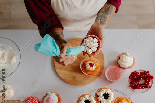 Top view of unrecognizable female confectioner decorating cakes while standing near the table