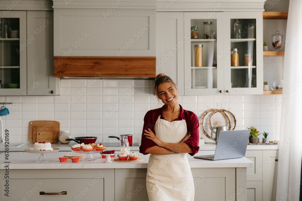 Joyful female baker looking confident while standing near the kitchen island with variety of sweet food Joyful female baker looking confident while standing near the kitchen island with variety of sweet food