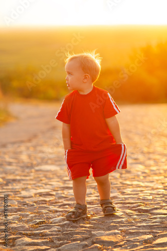 cute small boy silhouette walking on stone road in sunlight, child outdoors at sunset, childhood concept