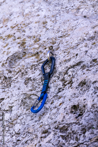 a blue and black climbing quickdraw clipped into a bolt in a limestone wall photo