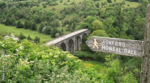 Footpath sign to Ashford Monsal Dale in front of the panoramic landscape looking down to the Monsal trail viaduct in Derbyshire Peak District. photo