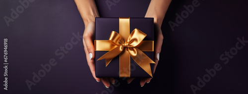 A holiday gift. Box in a dark gift wrapping with a gold bow, on a dark background. Merry Christmas, Happy New Year and other greetings. Postcard. High quality photo. High quality photo