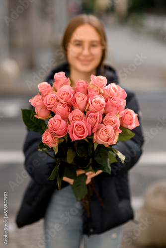 Young pretty dark-haired girl stands on a city street with a bouquet of pink roses