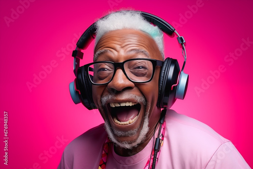 Homme noir senior, souriant, écoutant de la musique au casque avec un t-shirt coloré et un arrière-plan magenta photo