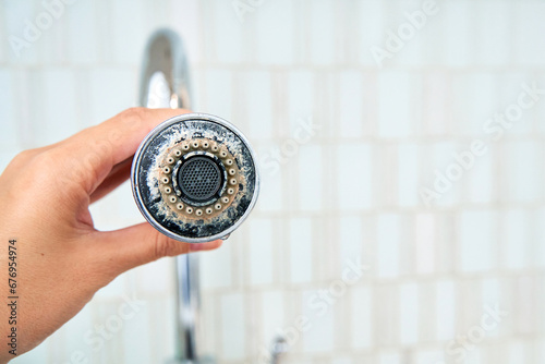 A woman is holding a chrome faucet covered with lime scale. photo