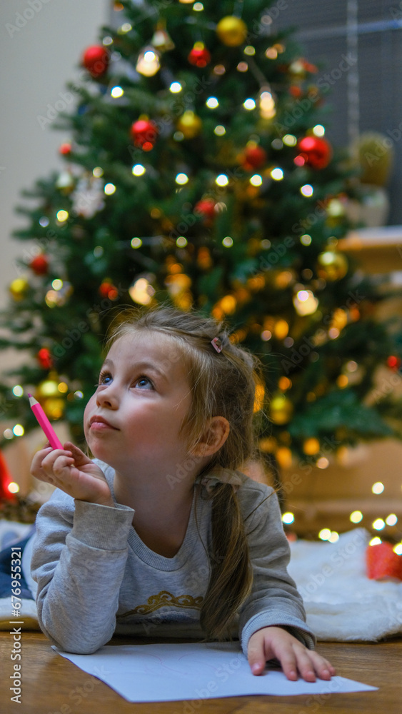 Special orders for Santa. Shot of a beautiful little girl smiling while writing a letter lying near the presents under the Christmas tree copyspace