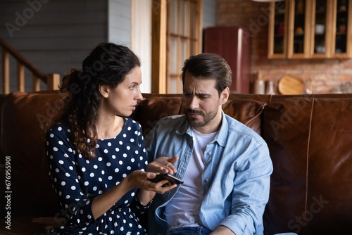 Fotografía Unhappy jealous woman arguing with man, holding smartphone, sitting on couch at
