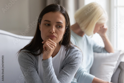 Annoyed selfish young woman ignoring unhappy mature mother after quarrel close up, parent and child, generations conflict, senior mum and grown daughter sitting back to back, misunderstanding photo