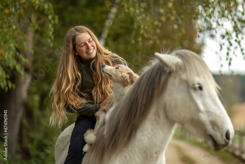 Horse and dog concept: A young female equestrian and her dog on her icelandic horse in front of a rural farm landscape