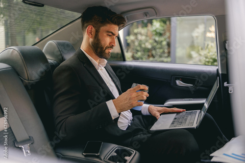 Professional male finansist working on laptop sitting car backseat and drinking coffee © Yaroslav Astakhov
