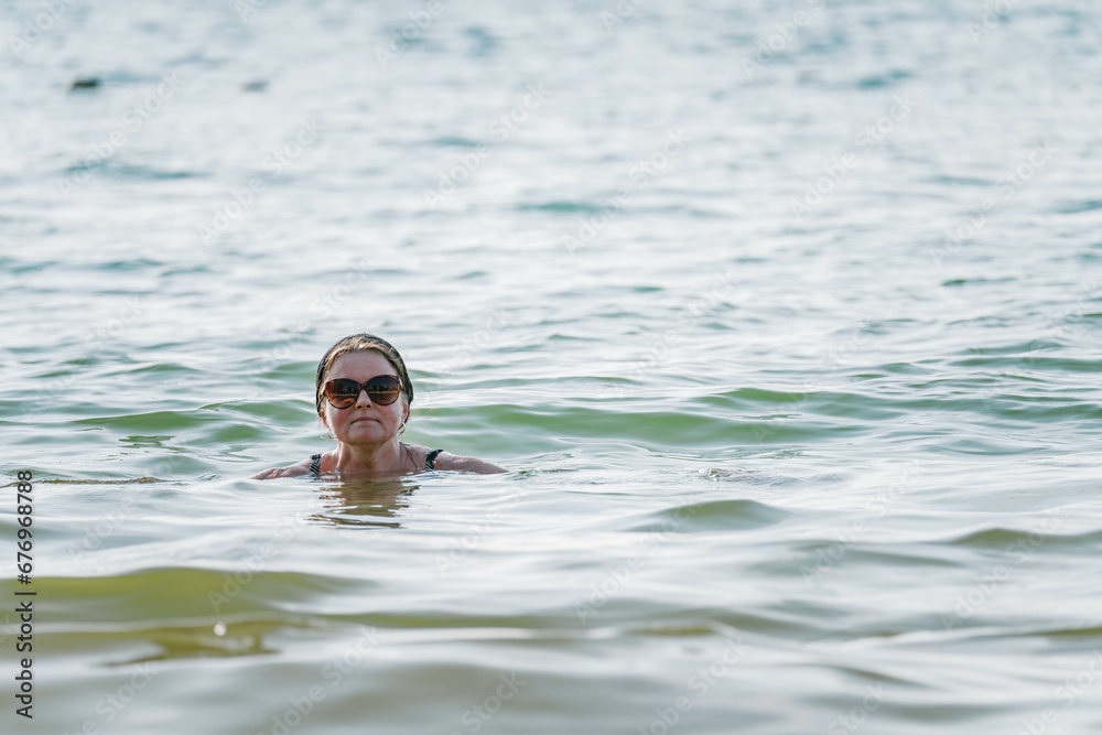 Attractive middle aged Scandinavian women in big sun glasses swimming in tropical sea, only head above a water, very close up photo