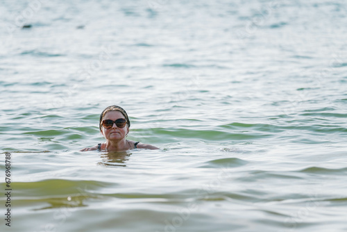Attractive middle aged Scandinavian women in big sun glasses swimming in tropical sea  only head above a water  very close up photo