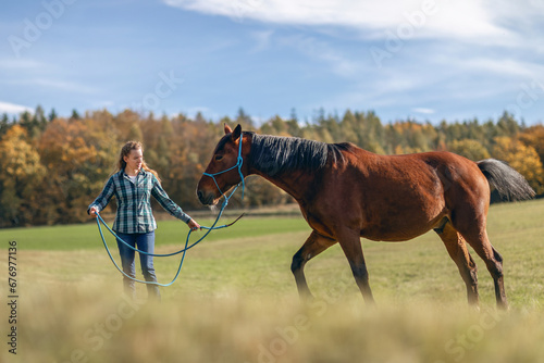 A female equestrian during basic work in natural horsemanship with her bay brown trotter horse in autumn on a meadow outdoors © Annabell Gsödl