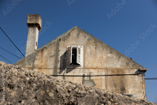 side of an old stone building in Croatia with an opened attic window against a blue sky on a hot summer afternoon