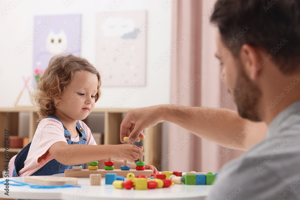Motor skills development. Father and daughter playing with stacking and counting game at table indoors Motor skills development. Father and daughter playing with stacking and counting game at table indoors