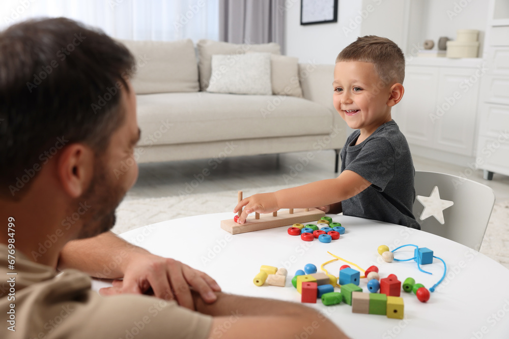 Motor skills development. Father and his son playing with stacking and counting game at table indoors Motor skills development. Father and his son playing with stacking and counting game at table indoors